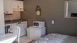 Habitación compacta con kitchenette, microondas, reloj, cama y una pequeña mesa.