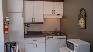 Una kitchenette compacta con gabinetes blancos, estufa, fregadero, cafetera y microondas.