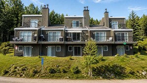 A multi-story residential building with balconies, large windows, and a grassy front yard.