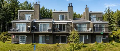 A multi-story residential building with balconies, large windows, and a grassy front yard.