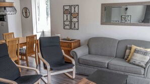 A living room with a sofa, chairs, a coffee table, a wooden side table, a clock, and a mirror on the wall.