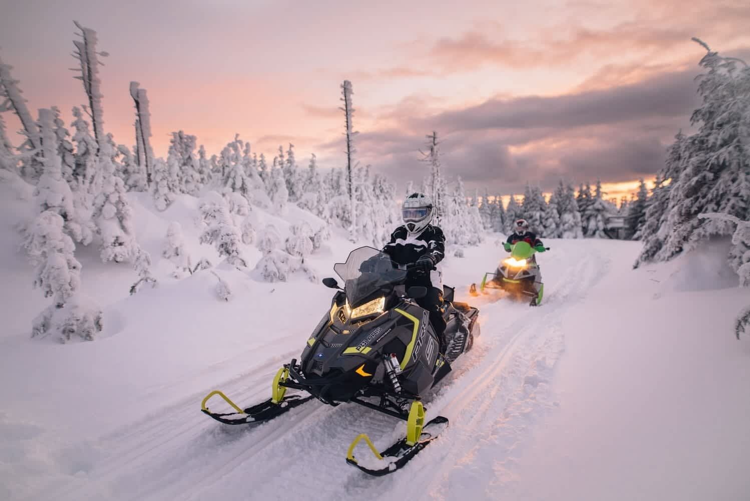 Two snowmobiles on a snowy path with snow-covered trees.