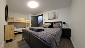 A bedroom with a bunk bed, a single bed, a nightstand, a lamp, and a framed picture on the wall.