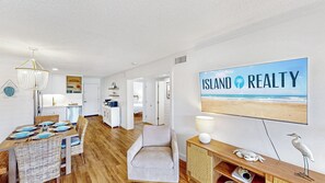 A spacious living area with a dining set, a comfortable seating area, and a large wall-mounted TV displaying 'ISLAND REALTY'.