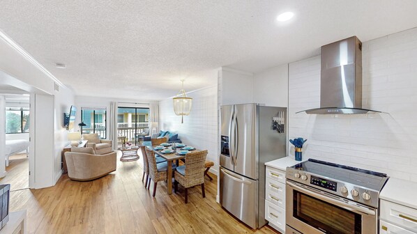 A modern kitchen with stainless steel appliances, a dining area with wicker furniture, and a balcony with a view.