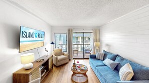 A modern living room with a flat-screen TV, a sofa, a coffee table, and a balcony with outdoor furniture.