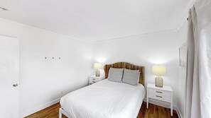 A bedroom with a bed, two bedside tables with lamps, a door, and a curtain.