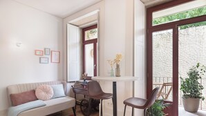 A cozy living area with a sofa, a small table, and chairs. There is a window with a view of greenery outside. - Loureiro 140 (Porto)