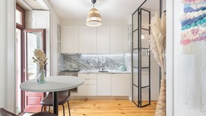 A modern kitchen with white cabinets, a marble countertop, and a round table with chairs. - Loureiro 140 (Porto)