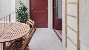 A wooden table and chairs outside a building with a red door and a window. - Loureiro 140 (Porto)