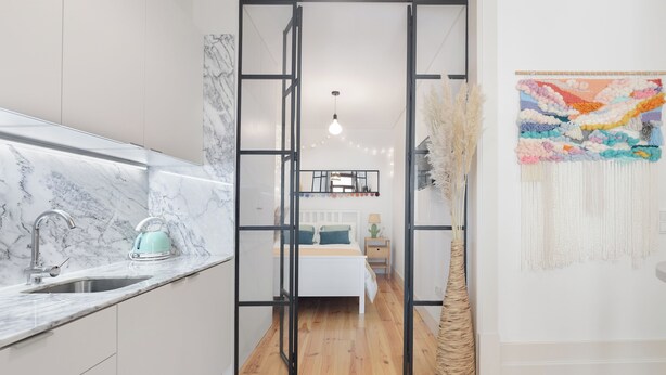 A modern kitchen with a marble countertop and a sink, leading to a bedroom with a bed and a nightstand. - Loureiro 140 (Porto)