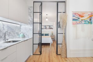 A modern kitchen with a marble countertop and a sink, leading to a bedroom with a bed and a nightstand. - Loureiro 140 (Porto)