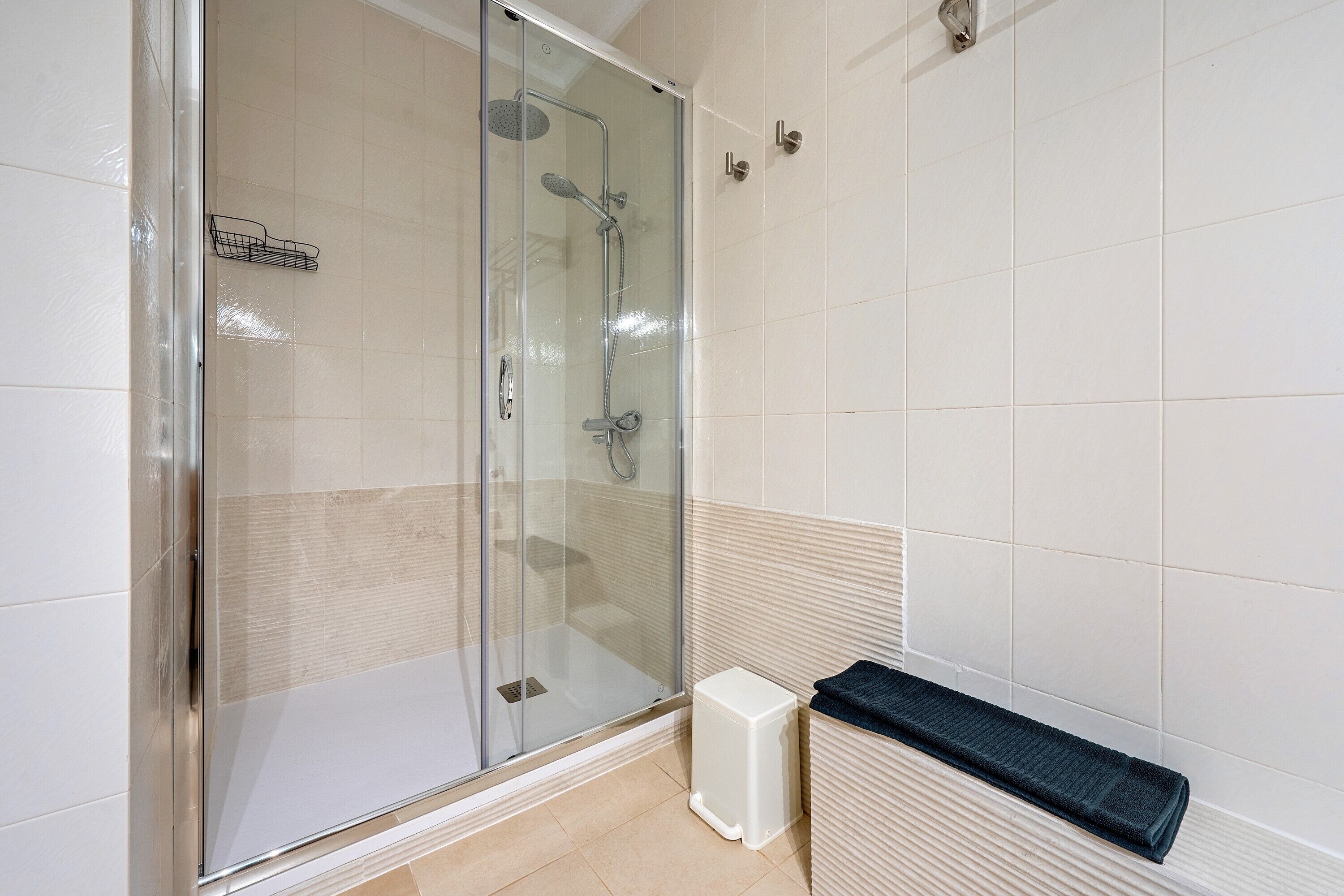 A modern bathroom with a glass-enclosed shower, a white pedestal sink, and a towel rack.