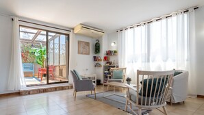 Un salon avec une porte-fenêtre coulissante donnant sur un balcon, un canapé, un fauteuil, une petite table et une bibliothèque.