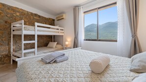 Une chambre avec des lits superposés, une grande fenêtre donnant sur la montagne et un mur en pierre.