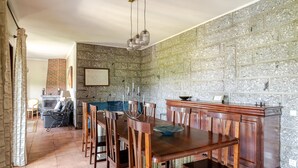 Een eetgedeelte met een grote houten tafel, stoelen, een stenen muur en een open haard.
