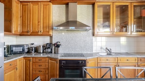 Een keuken met houten kastjes, een roestvrijstalen afzuigkap, een magnetron, een koffiezetapparaat en een spoelbak.