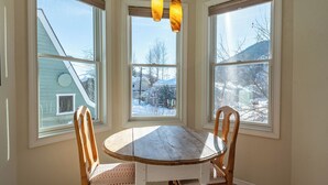 Un comedor con una mesa y sillas de madera, ventanas amplias con vistas a un paisaje nevado y una lámpara colgante.