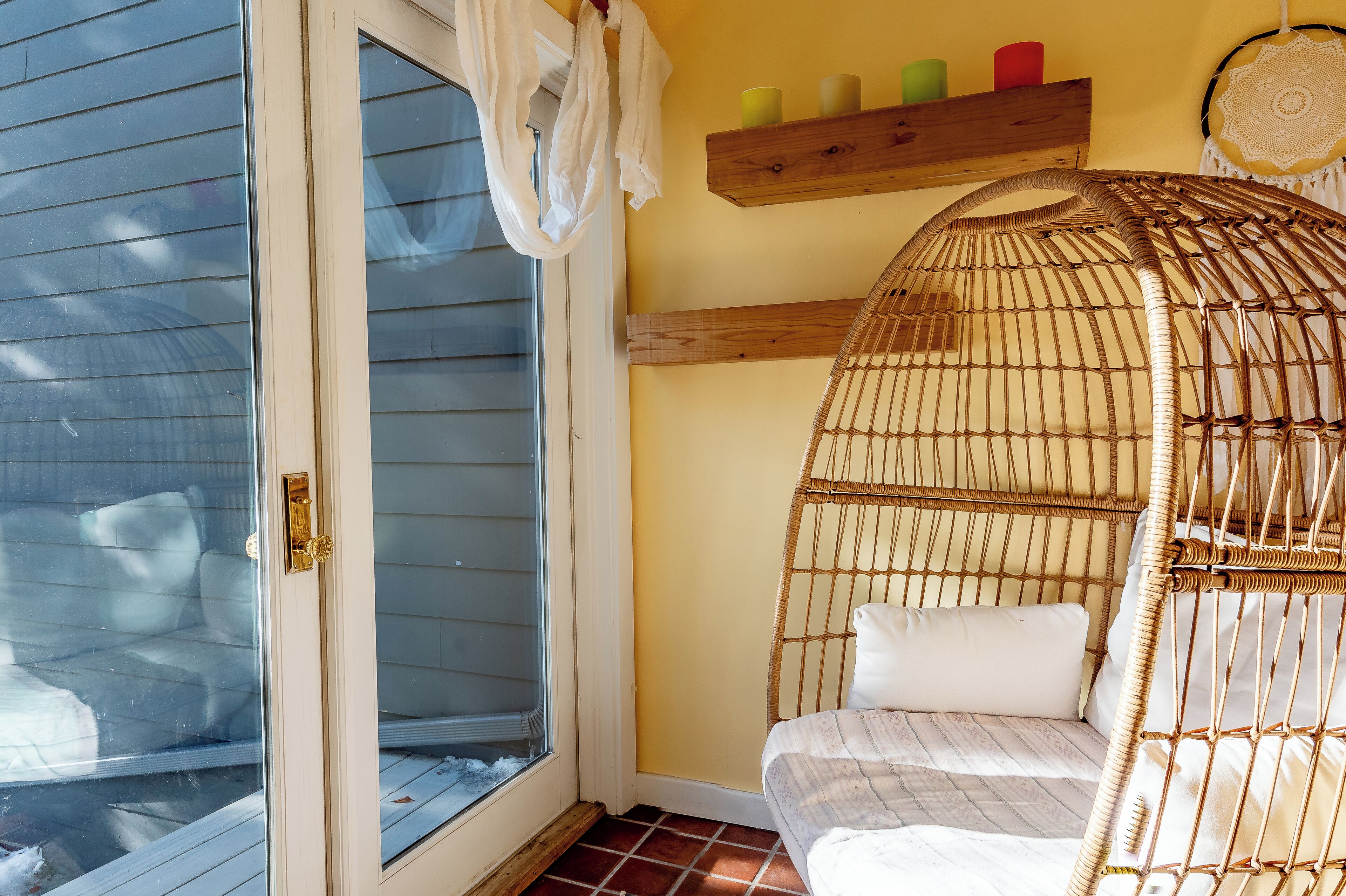 Une chambre avec un lit en osier, une porte-fenêtre coulissante, une étagère en bois ornée de bougies et une tête de lit en fibres tressées.
