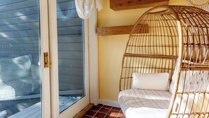 Una habitación con una cama de mimbre, puerta corredera de vidrio, estante de madera con velas y cabecera tejida.