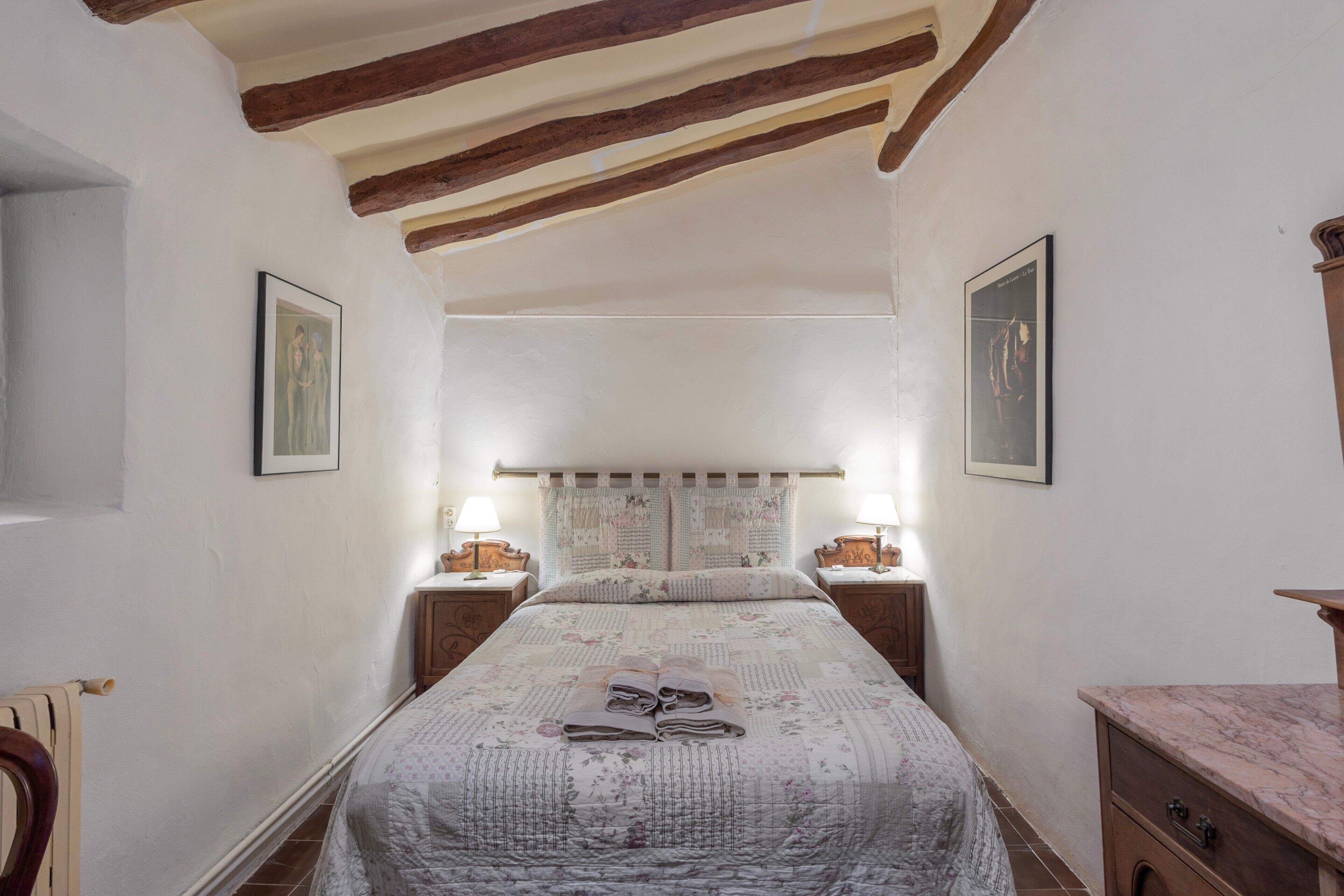 A bedroom with a bed, two bedside tables, a nightstand, a wooden headboard, and a marble side table.