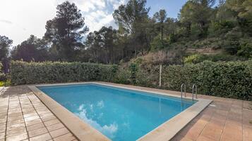 Piscina retangular com deck ladrilhado, rodeada por um sebedo e árvores.