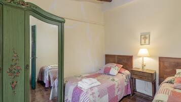 A bedroom with two beds, a wooden wardrobe, a bedside table with a lamp, and a framed picture on the wall.
