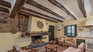 Um interior rústico com vigas de madeira aparentes, lareira, móveis de vime e uma área de cozinha.