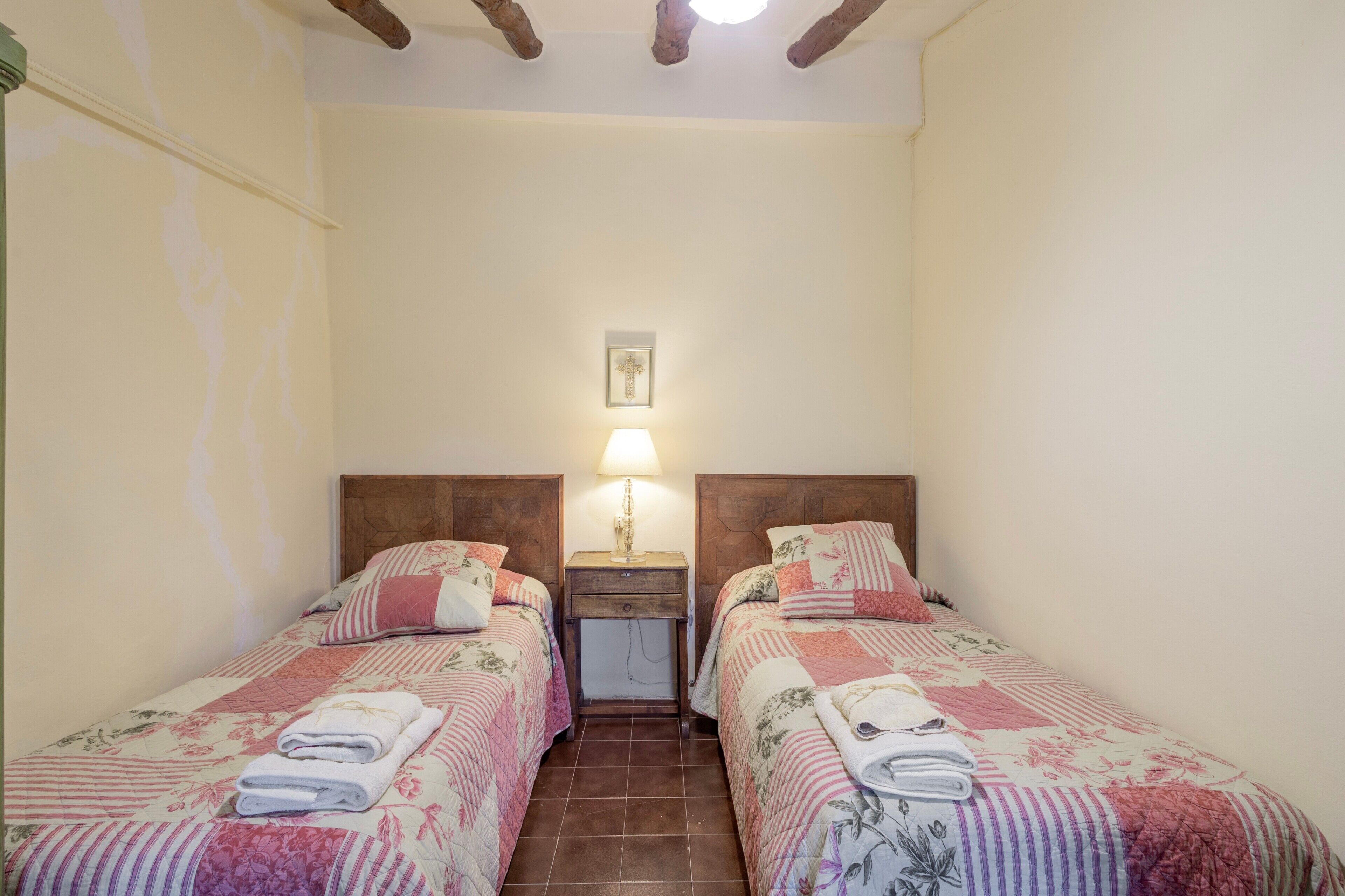 Une chambre avec deux lits, une table de chevet, une lampe et un crucifix fixé au mur.