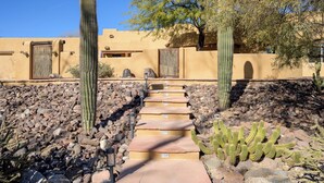 Un sendero conduce a un edificio de fachada amarilla, rodeado de cactus y rocas.
