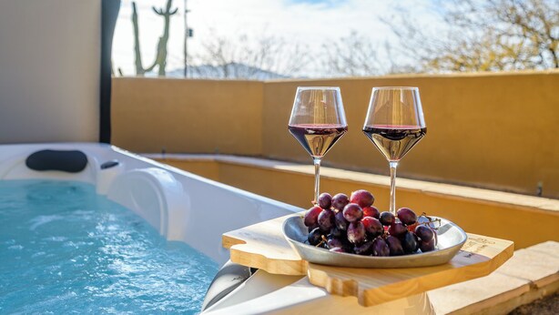 Un jacuzzi con dos copas de vino tinto y un cuenco de uvas sobre una mesa de madera.