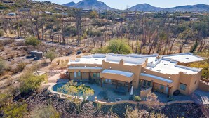 Una casa grande y moderna con piscina y varias habitaciones, rodeada de un paisaje montañoso y seco.
