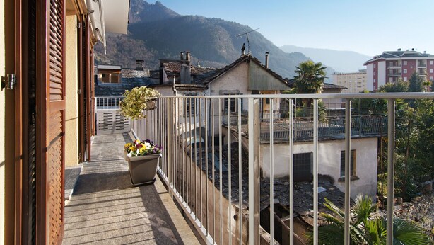 Un balcón con vista a una montaña, un edificio pequeño y una barandilla.