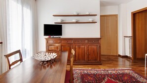 Un comedor con una mesa de madera, sillas, un cuenco decorativo, un televisor de pantalla plana y estantes de madera sobre la encimera.