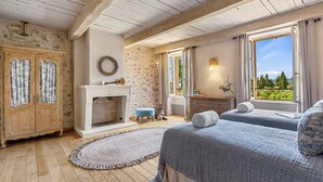 A bedroom with a fireplace, wooden floors, a large window with a view, and a wardrobe.