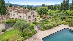 A stone building with a swimming pool, surrounded by lush greenery and a view of distant mountains.