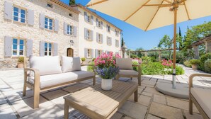 A stone building with a courtyard patio featuring outdoor furniture and a large umbrella.