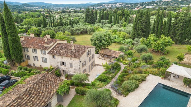 A villa with a swimming pool, surrounded by lush gardens and tall cypress trees.