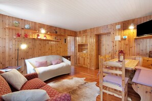 A wooden-paneled room with a sofa, a dining table with chairs, and a television.