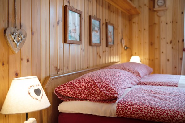 A wooden paneled room with a bed, pillows, a heart-shaped lamp, and framed pictures on the wall.