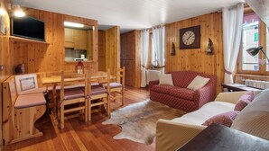 A wooden interior with a dining table, chairs, a sofa, a television, and a clock on the wall. - Apartment 'Corti Garden' with Mountain View, Private Garden and Wi-Fi (Campodolcino)