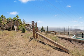 A fenced outdoor area with a wooden structure, possibly a playground, and a view of a cityscape in the background. - 'Finca Verónica' with Sea View, Wi-Fi and Air Conditioning (Candelaria)