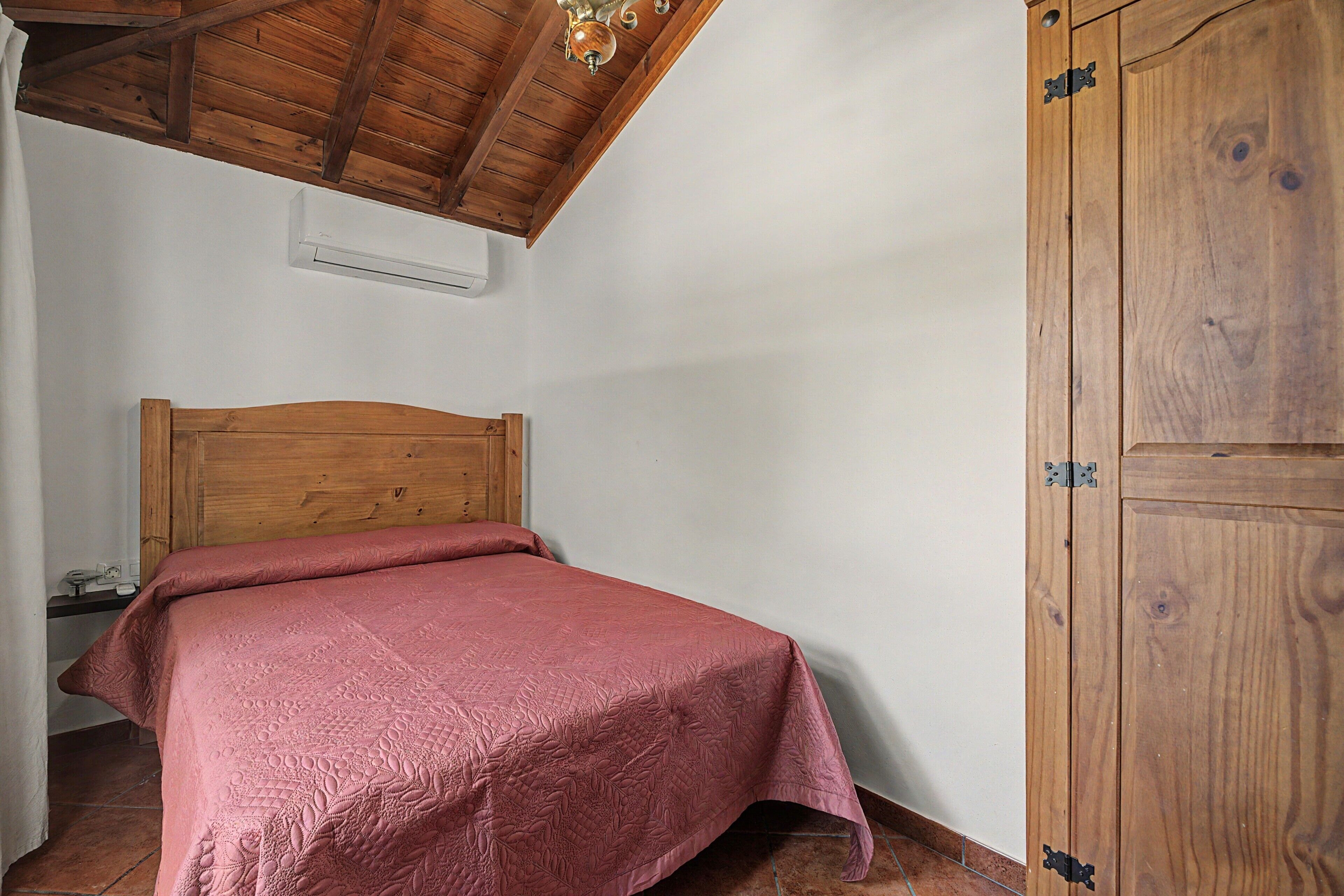 Een slaapkamer met een houten bed, een kledingkast en een airconditioner.
