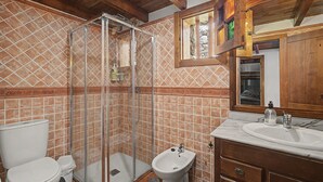 Een badkamer met een douche, toilet, bidet en een wastafel met spiegel.