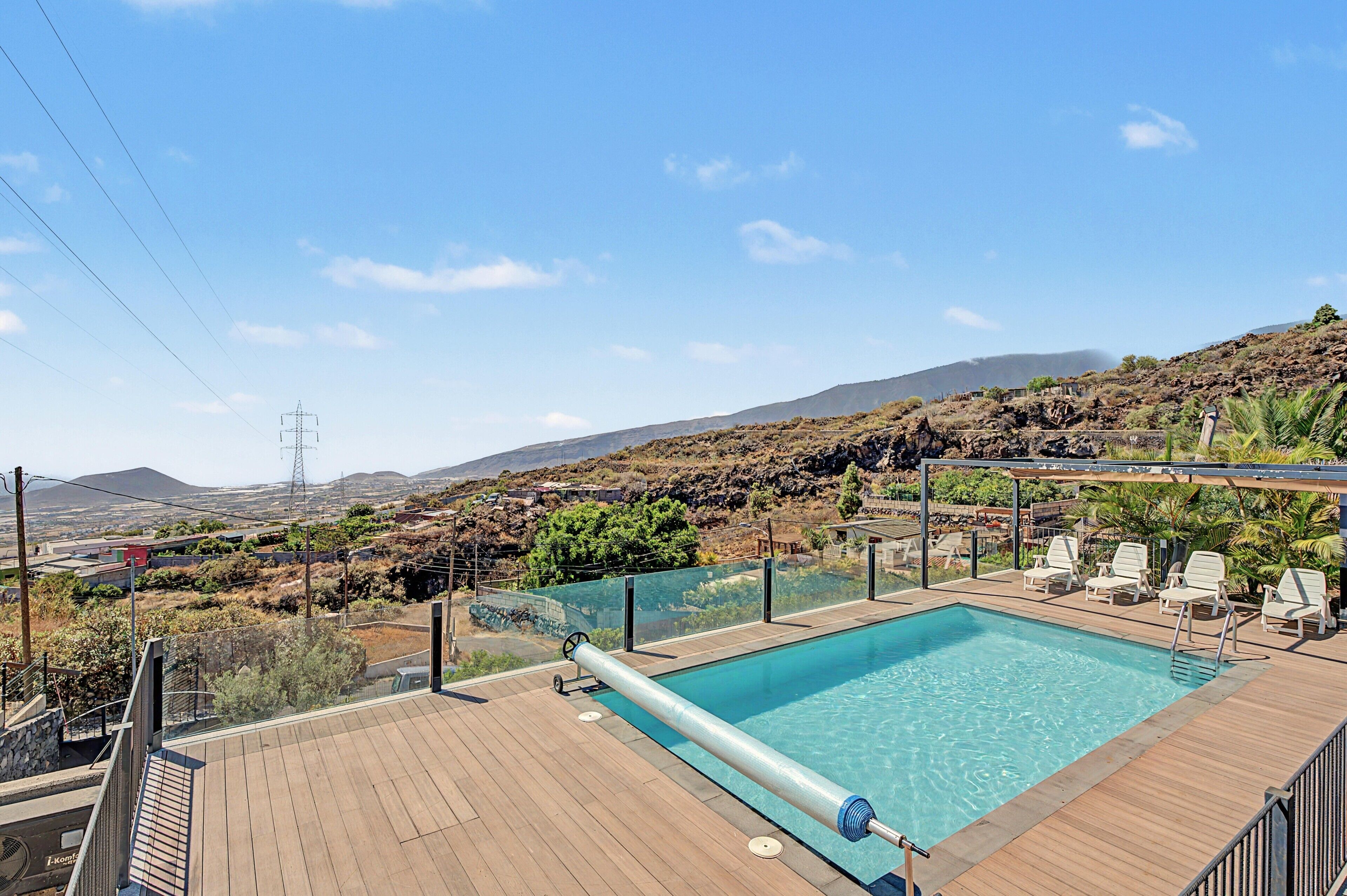 Una piscina con vistas a un paisaje montañoso, rodeada por una terraza de madera y sillas de descanso.