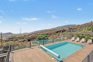 A swimming pool with a view of a mountainous landscape, surrounded by a wooden deck and lounge chairs. - 'Finca Verónica' with Sea View, Wi-Fi and Air Conditioning (Candelaria)