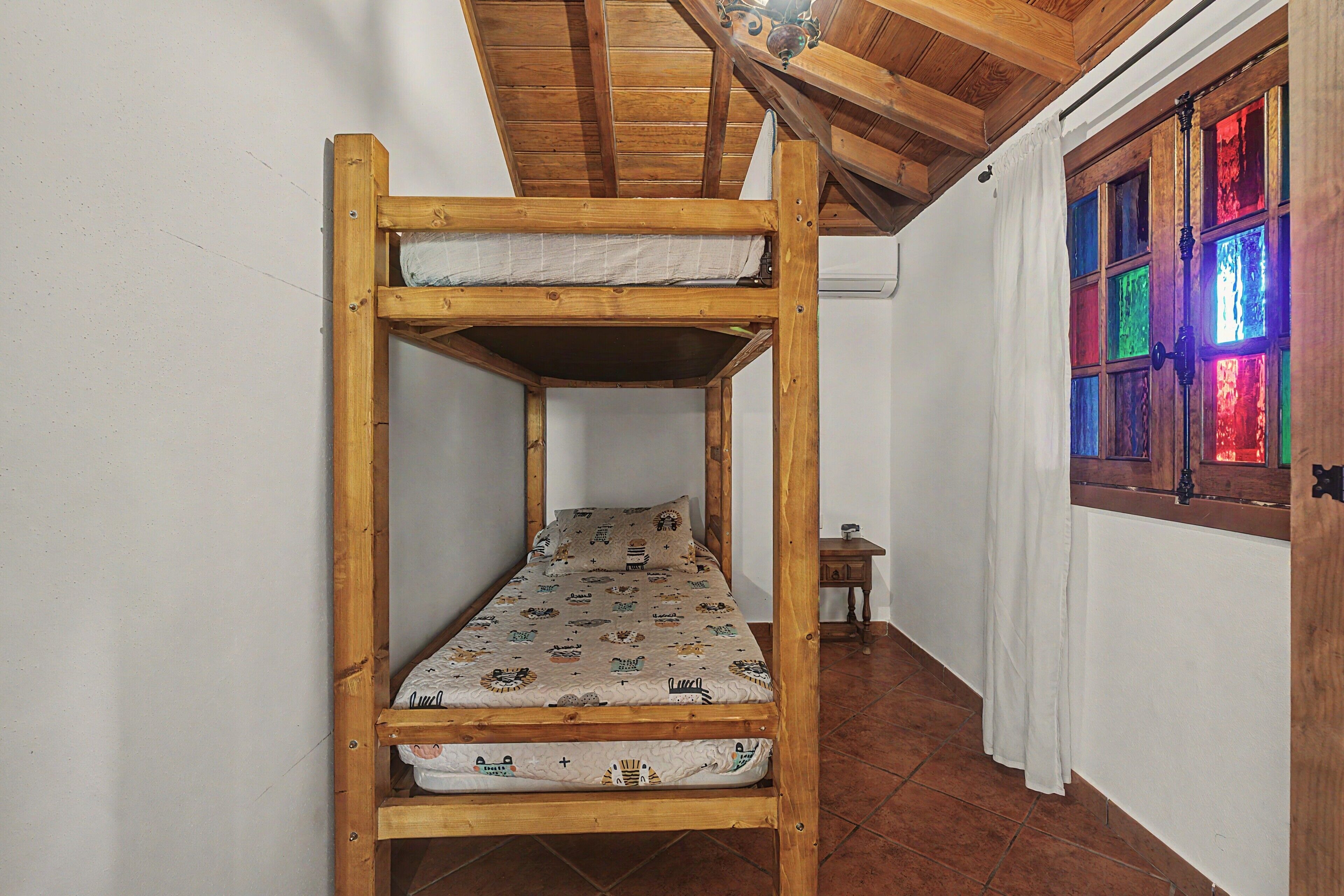 Un lit superposé avec un matelas à motifs, une tête de lit en bois et une fenêtre ornée de vitraux colorés.
