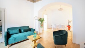 A modern living room with a teal sofa, a wooden coffee table, and a dark armchair. There is a dining area with white chairs and a table in the background. - City Center- Modern and Bright apartment (Rome)