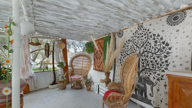 Una habitación con una silla de fibras naturales, un tapiz en la pared y una planta en maceta.