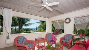 A sunlit room with wicker furniture, a ceiling fan, and a view of the ocean. - Indigo 2br 2 Bedroom Home (Governor's Harbour)